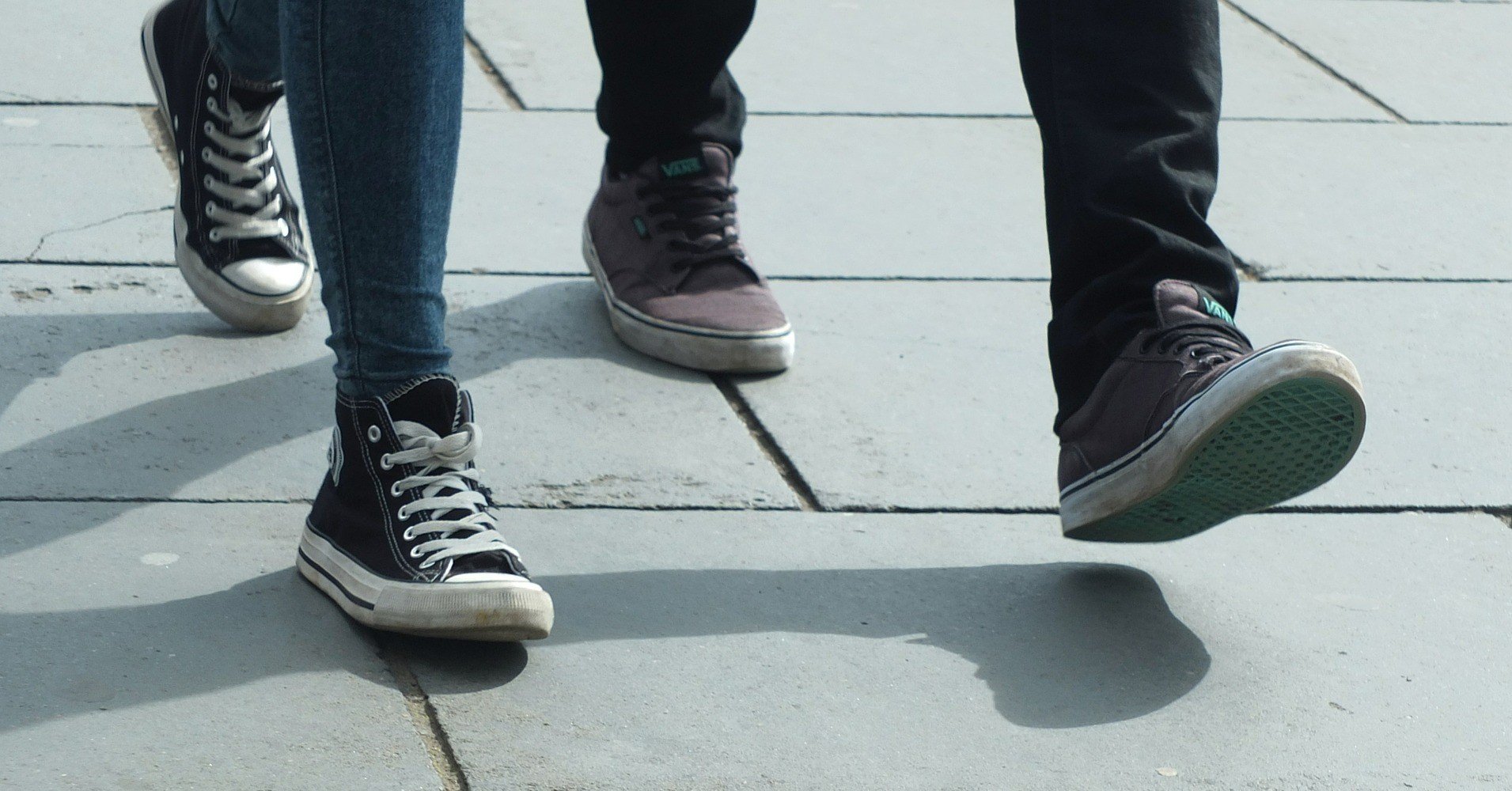 Two pair of legs in sneakers walking on a pavement.