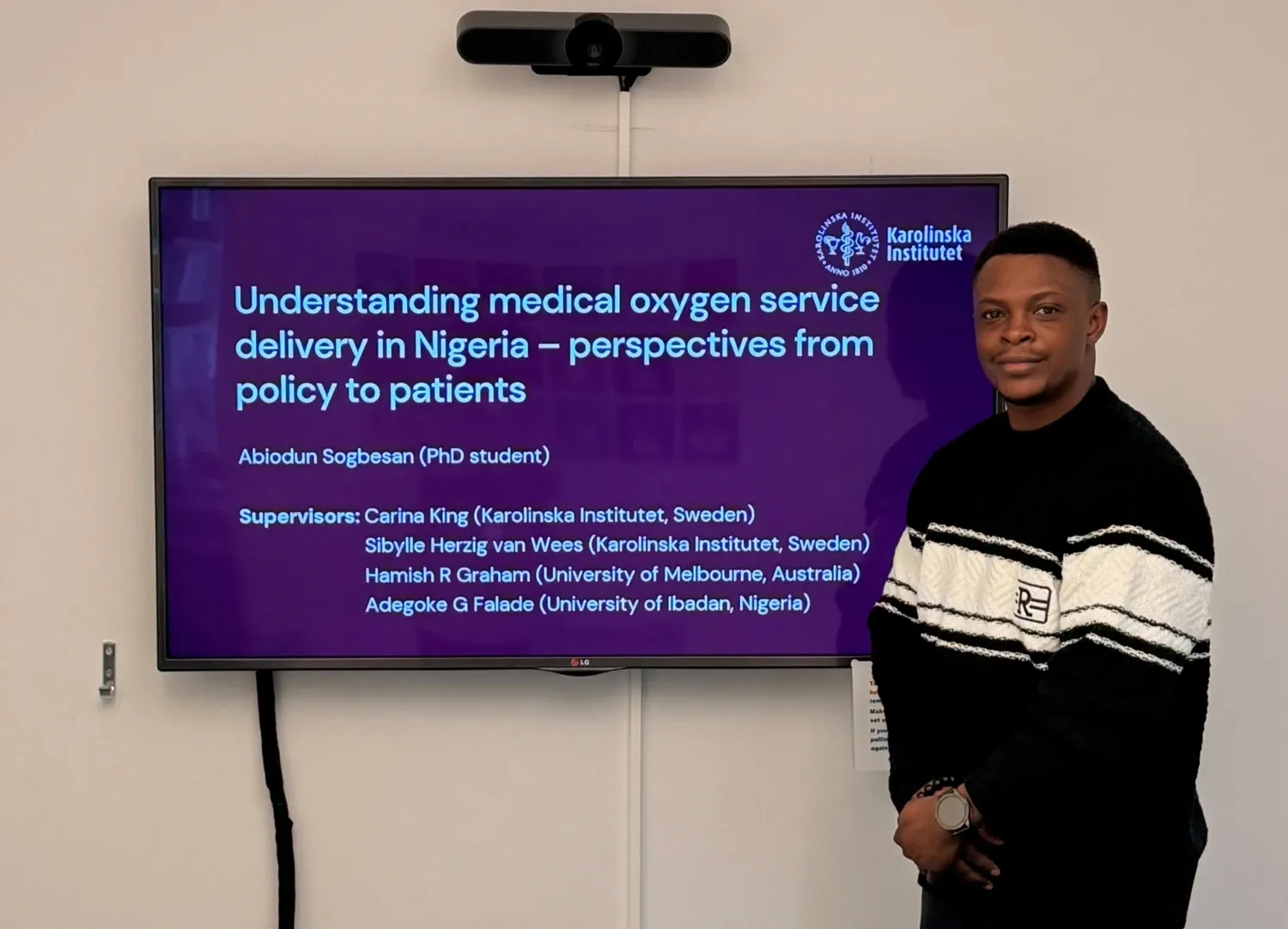 Abiodun Sogbesan standing by a large wall screen presenting his research.