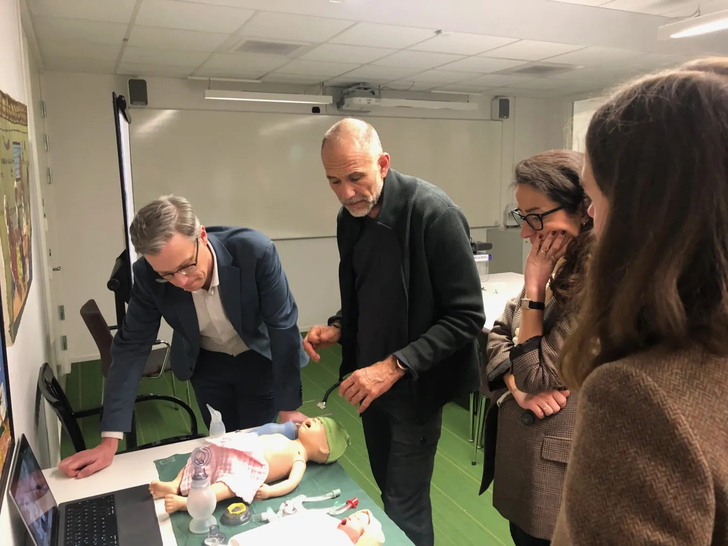 Three persons practice how to ventilate a newborn in a simulation exercise with a doll.