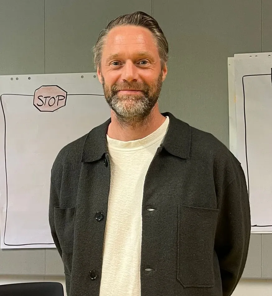 A portrait of a man with blond hair, wearing a white T-shirt and a black cardigan