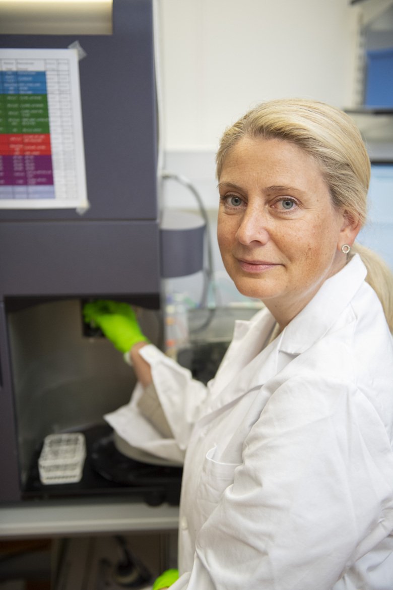 Portrait of Anna Smed Sörensen in the lab. She is blond, has a white lab coat and green gloves.