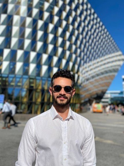 Man in sunglasses standing in front of a building looking straight into the camera