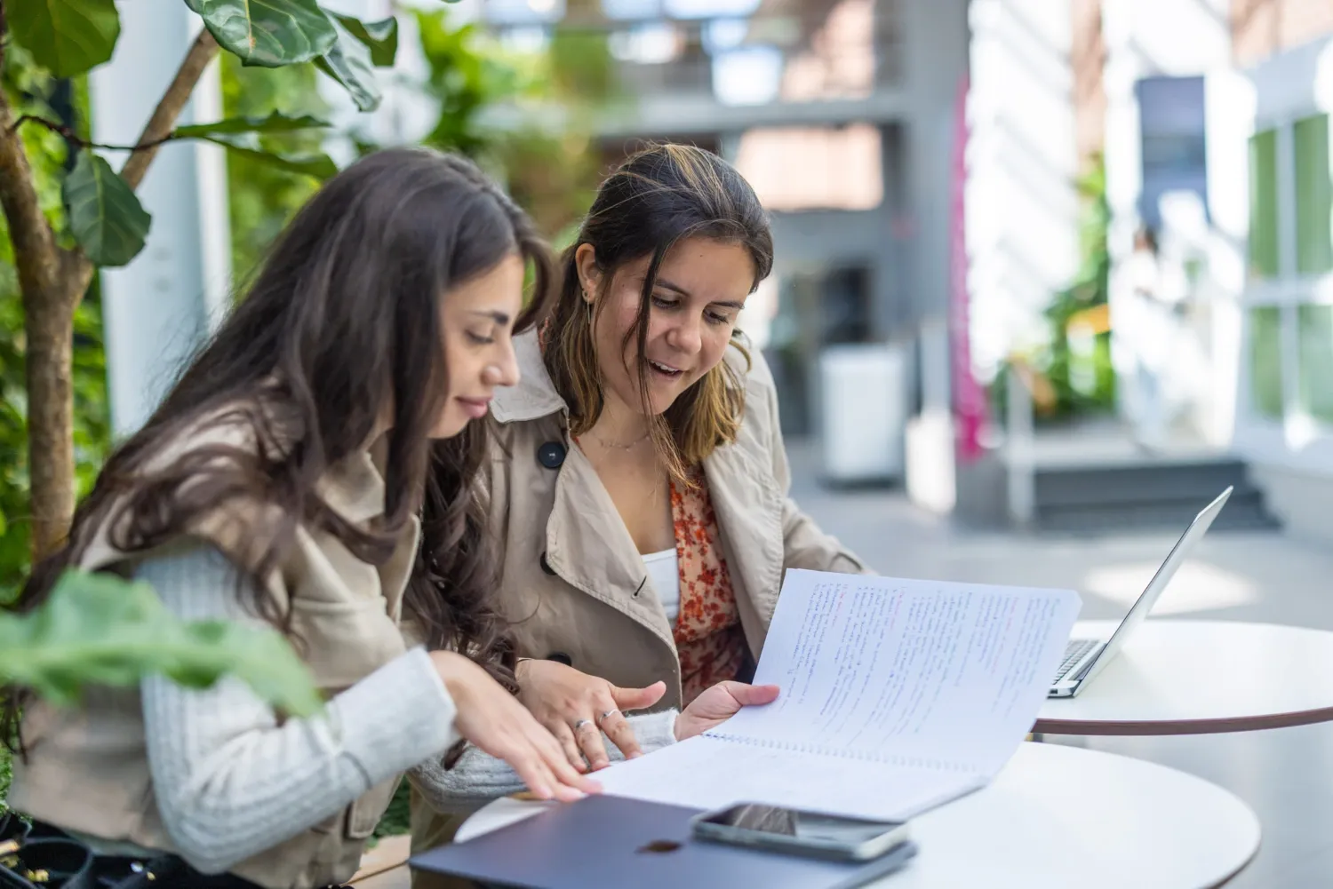 Students indoors at campus Solna during the spring semester of 2022. || Students sitting in an open area indoors studying with their laptops in their lap.