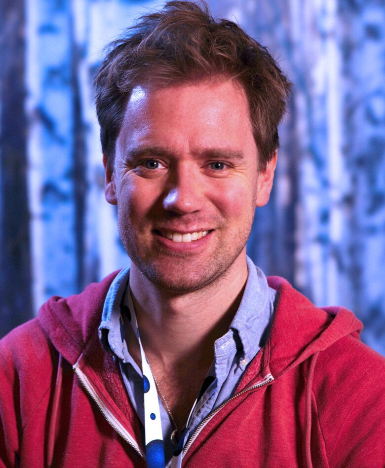Portrait of Eric Thelin against blue backdrop in a red hoodie.