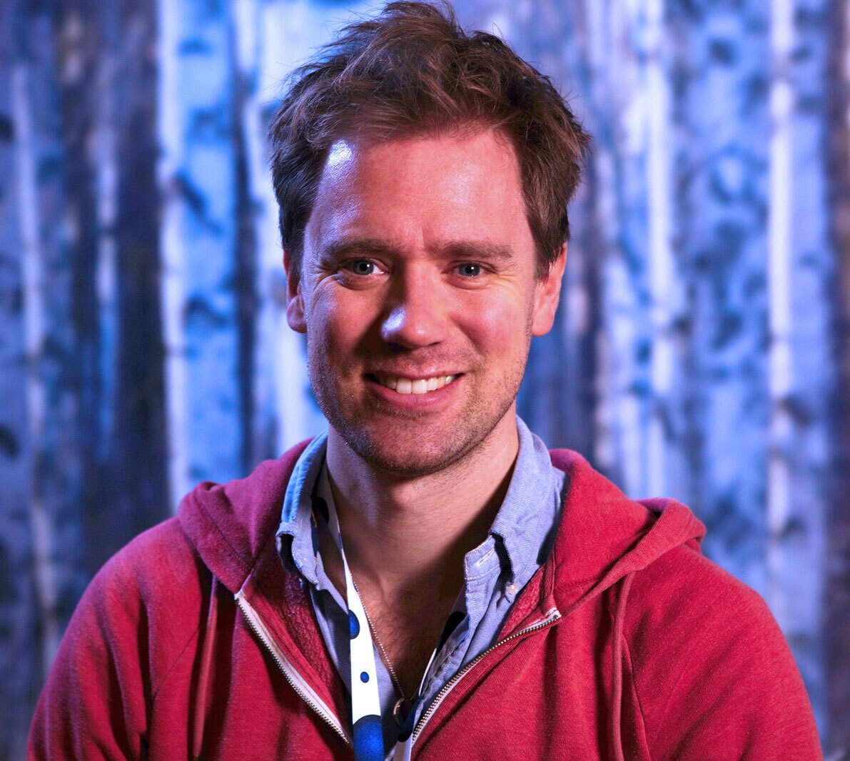 Portrait of Eric Thelin against blue backdrop in a red hoodie.