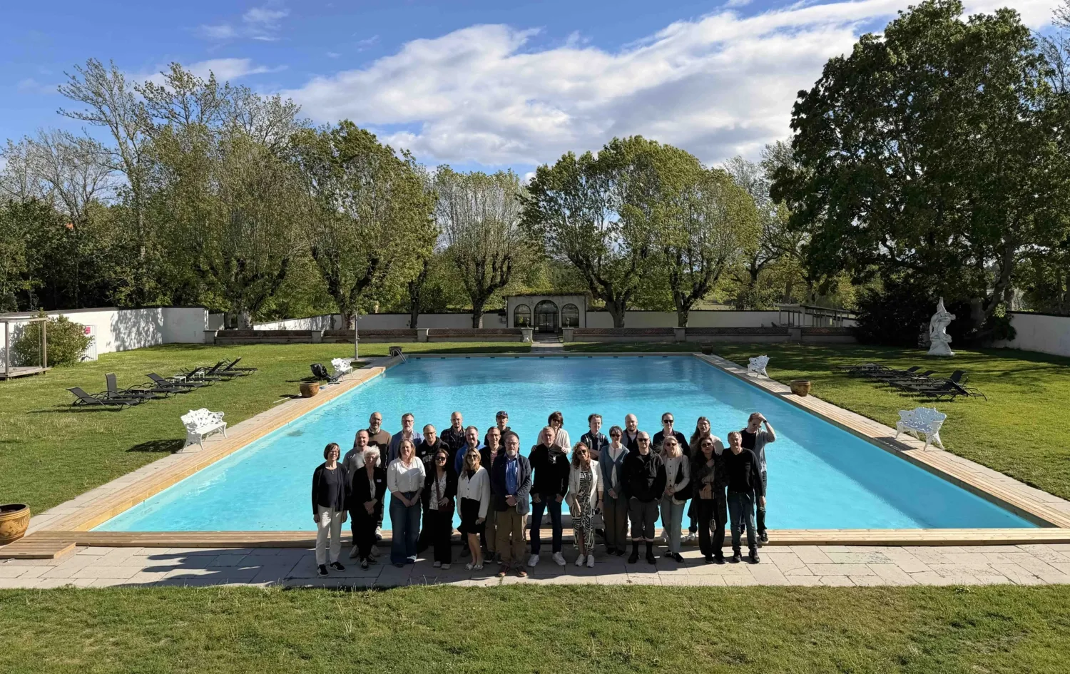 A group photo of around 20 people standing in front of a swimming pool at a conference centre.