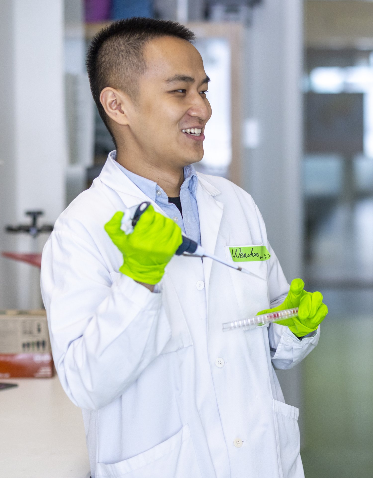 Man and woman standing in lab environment talking. The man is holding a pipette.