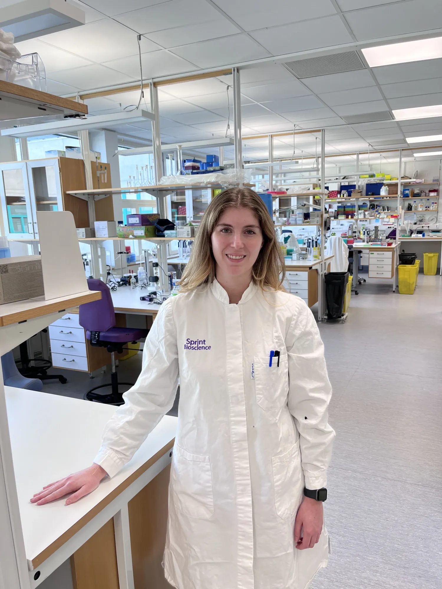 Woman wearing a white lab coat, standing in a lab.