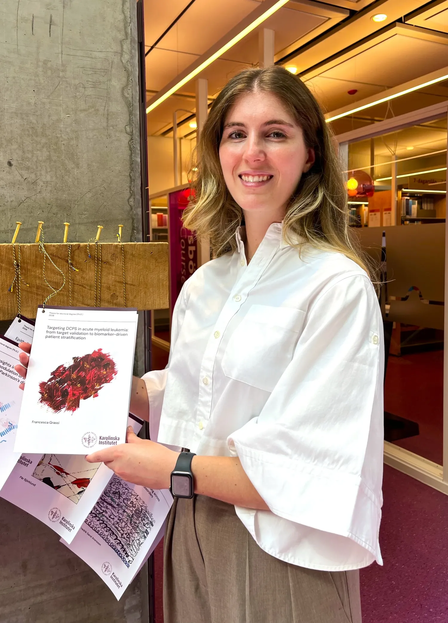 A portrait of a woman in a white shirt. She is holding up a thesis towards the camera.