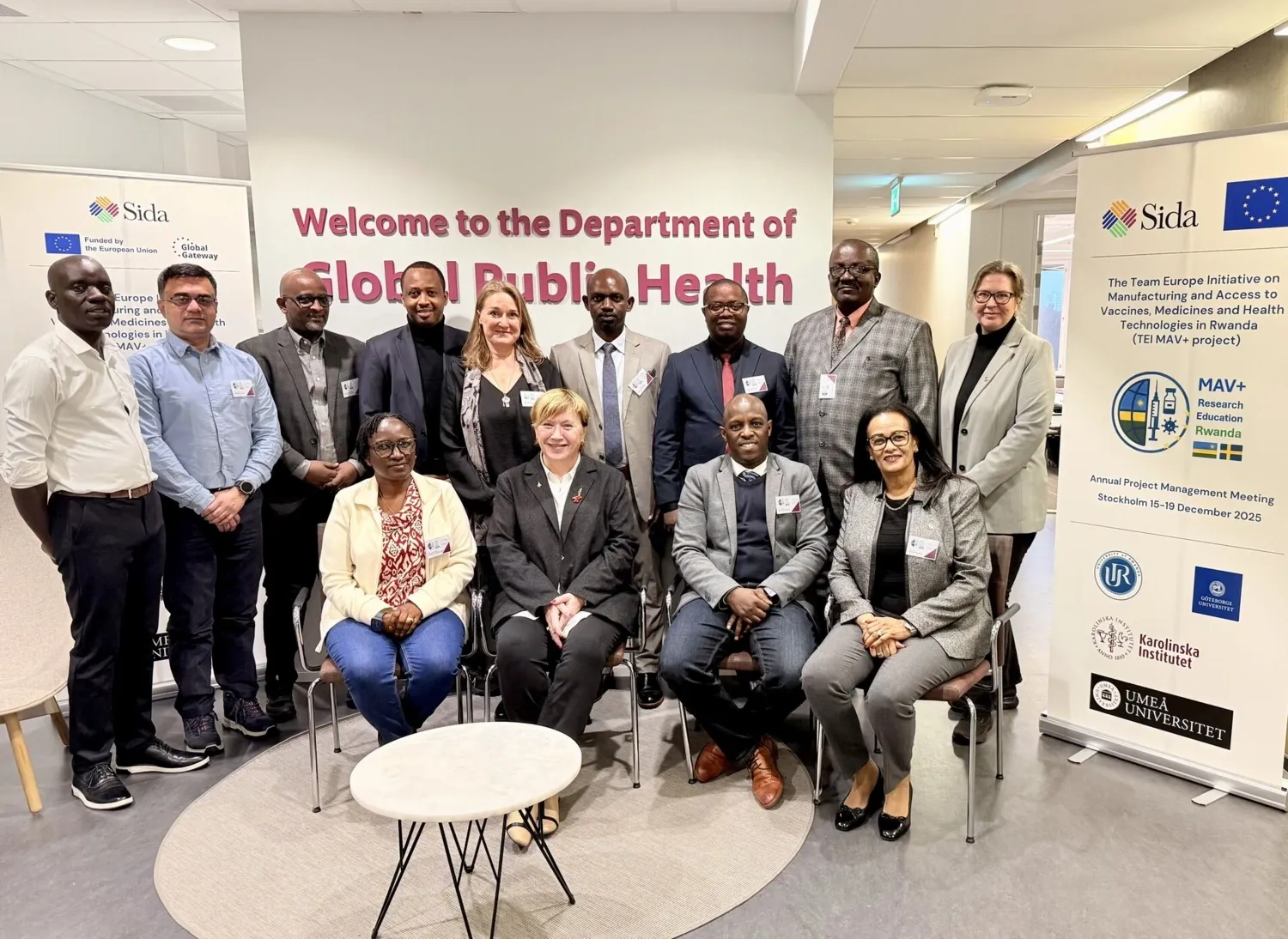 12 persons in a group photo in front of a wall sign saying Welcome to the department of global public health.