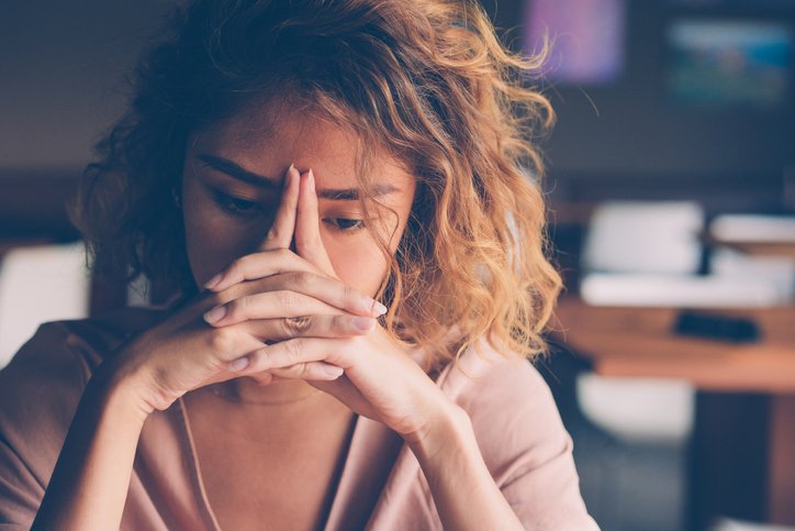 Closeup of sad and tired young woman at a cafe leaning her head on clasped hands