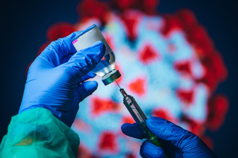 Person with gloves holds vaccine syringe.