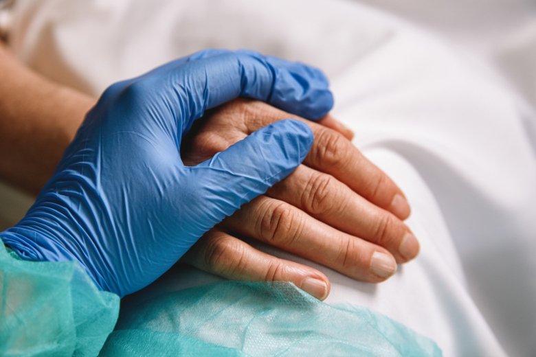 Medical staff in protective glove holds hand over patient's hand.