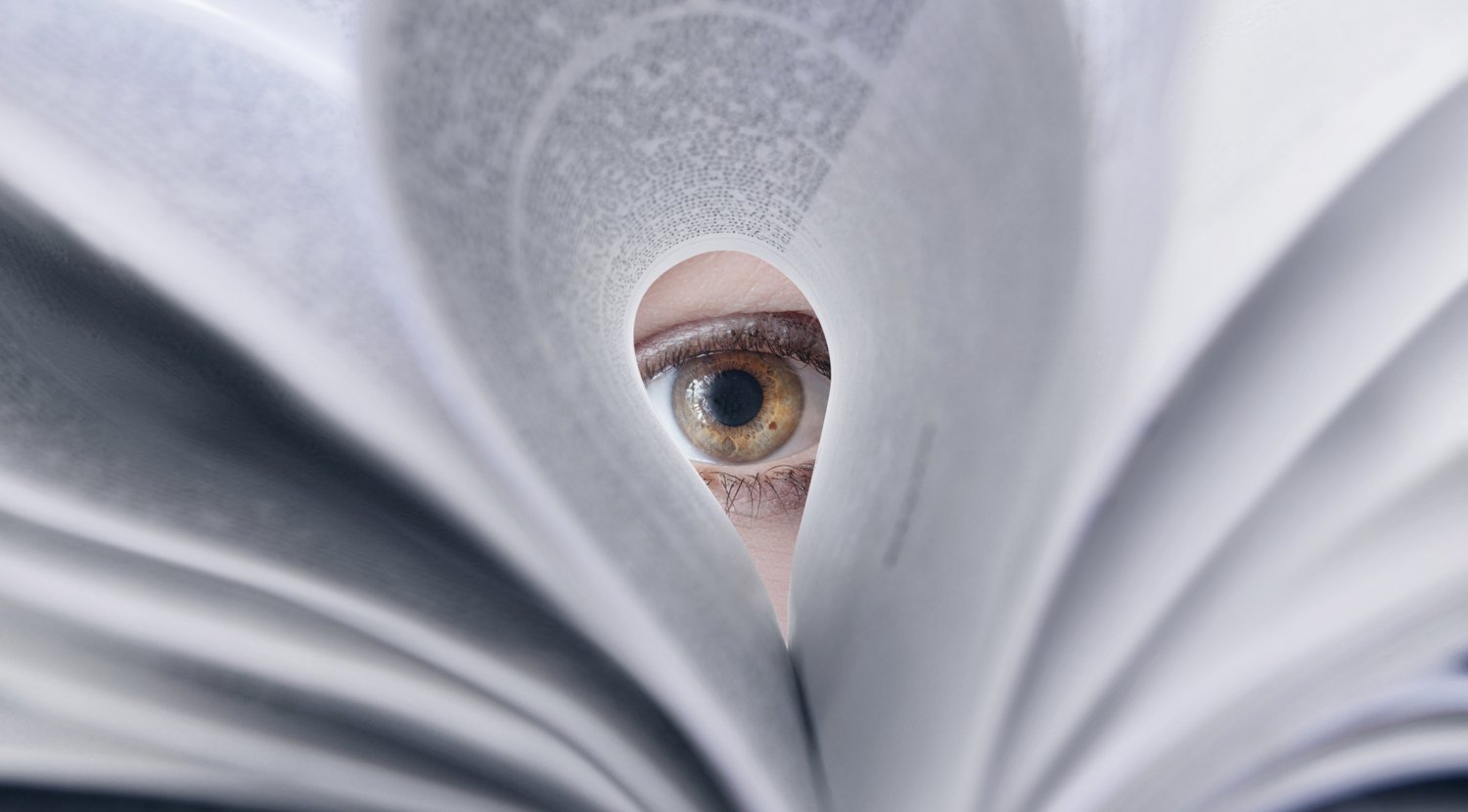 An eye looking through a folded book page.