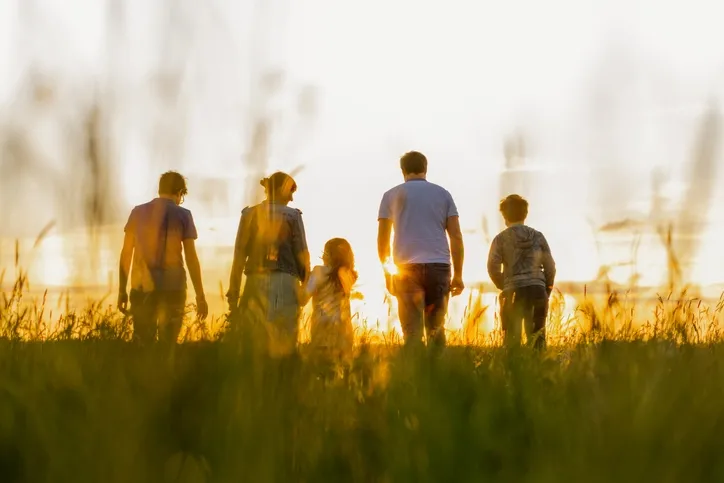 A family holding hands as they walk along a beach toward the water, seen from behind.