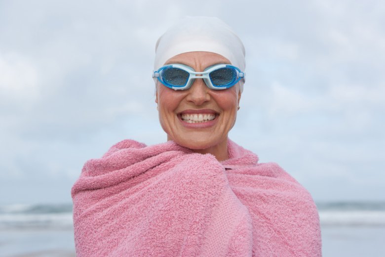 Smiling woman with bath towel coming from the sea.