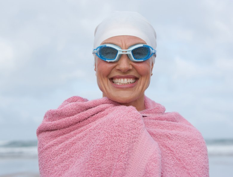 Smiling woman with bath towel coming from the sea.