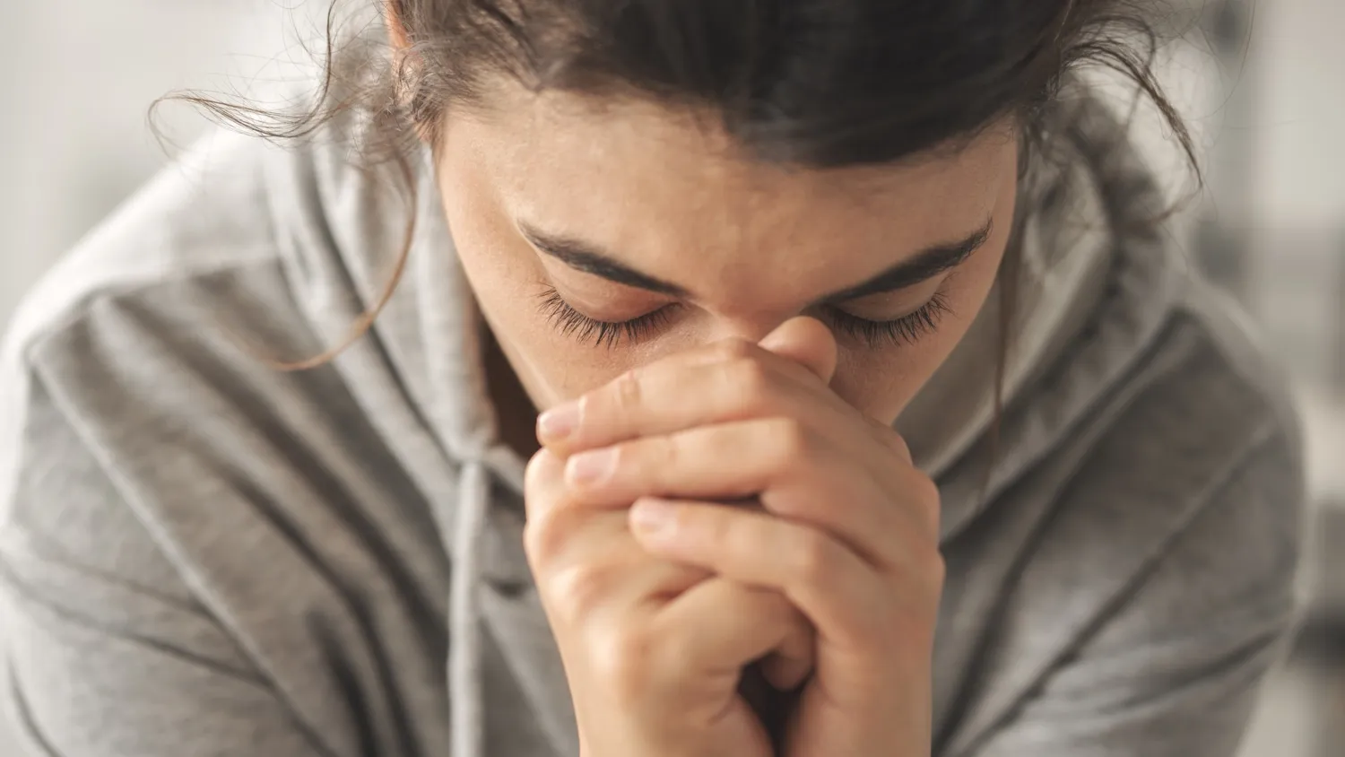 Person with hands clasped in front of their face, head bowed.