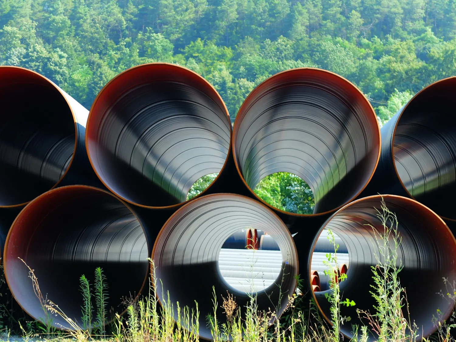 Metal pipes placed on top of each other. A green landscape is visible through the pipes.