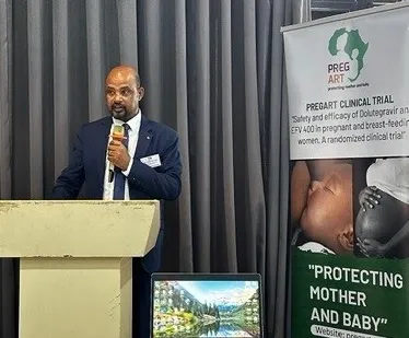 Am and stading by a podium speaking. By his side is a roll-up with Pregart project information.