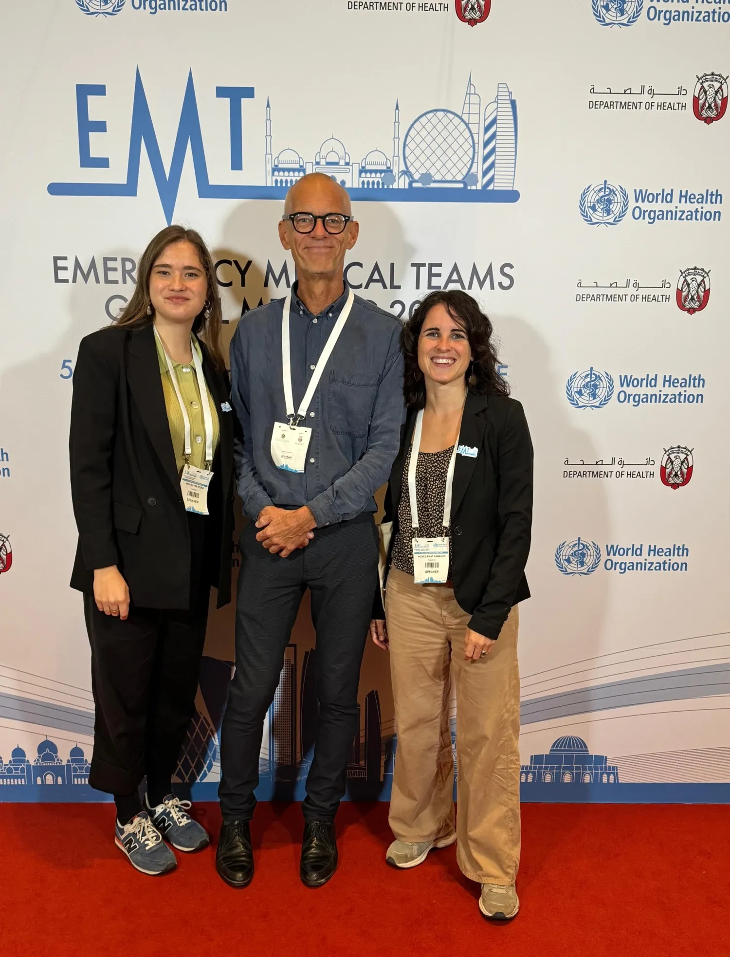 Three people, a man and two women, standing infront of a screen with the WHO's logo