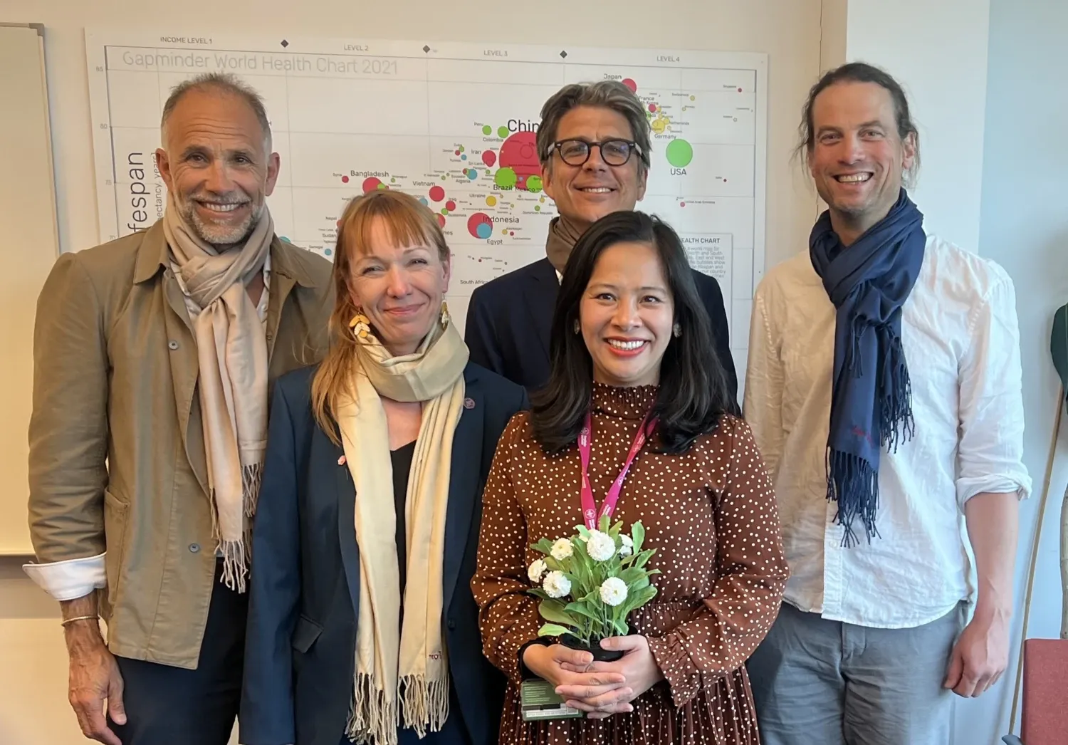 Two women and three men posing for the photo. The woman in the middle holds a bouquet of flowers.