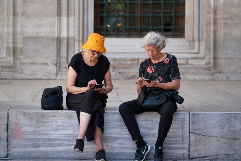Two old women using their smart phones in  a vacation setting.