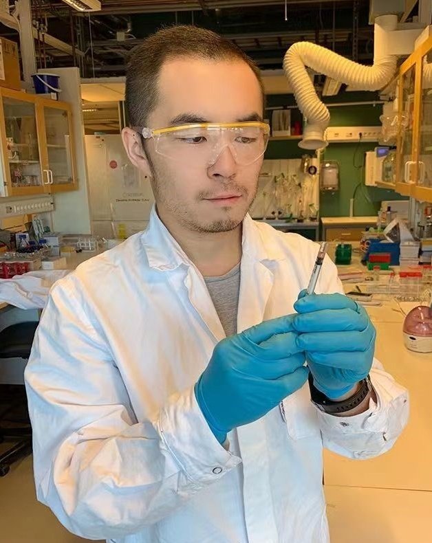 Photo of man in a lab coat, glasses and blue gloves.