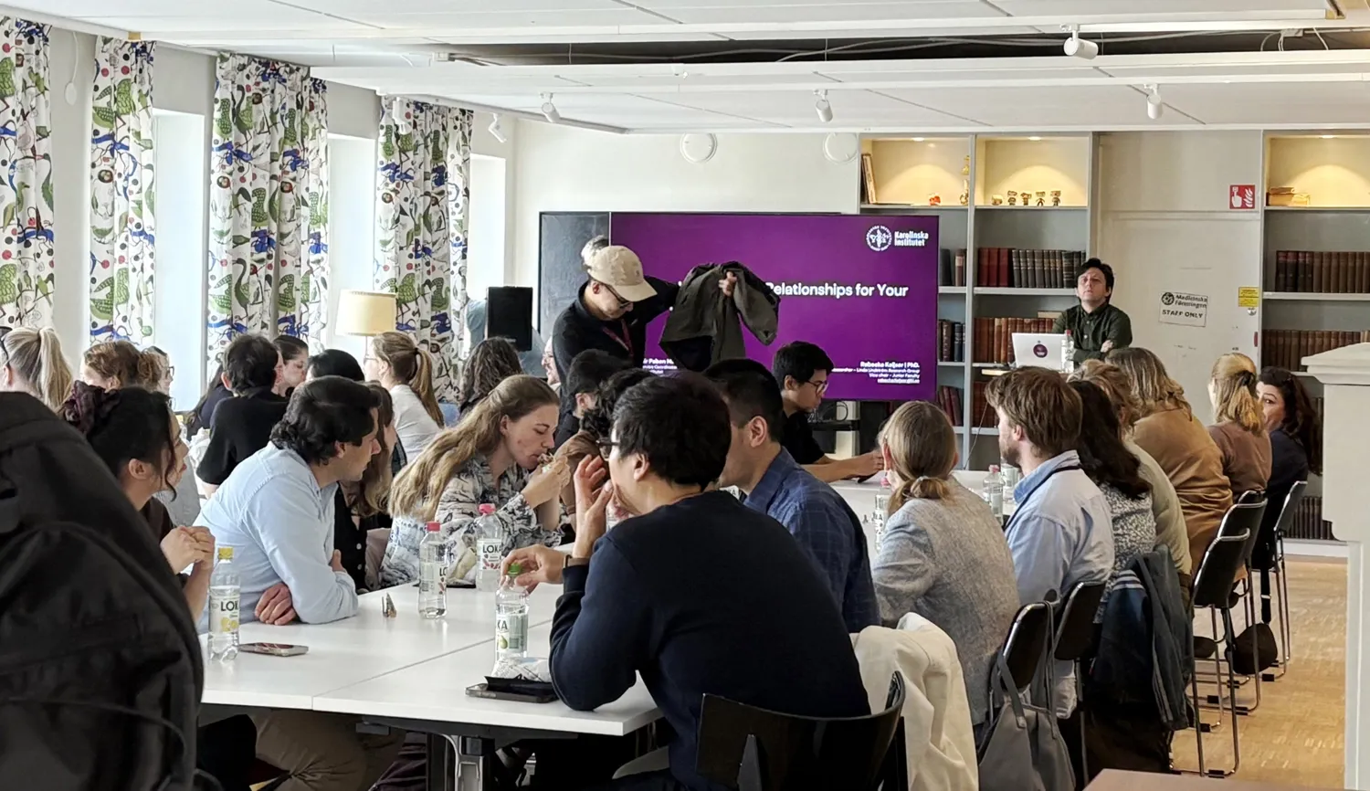 A photo from an after-work showing participants seated at tables, with a small stage at the front