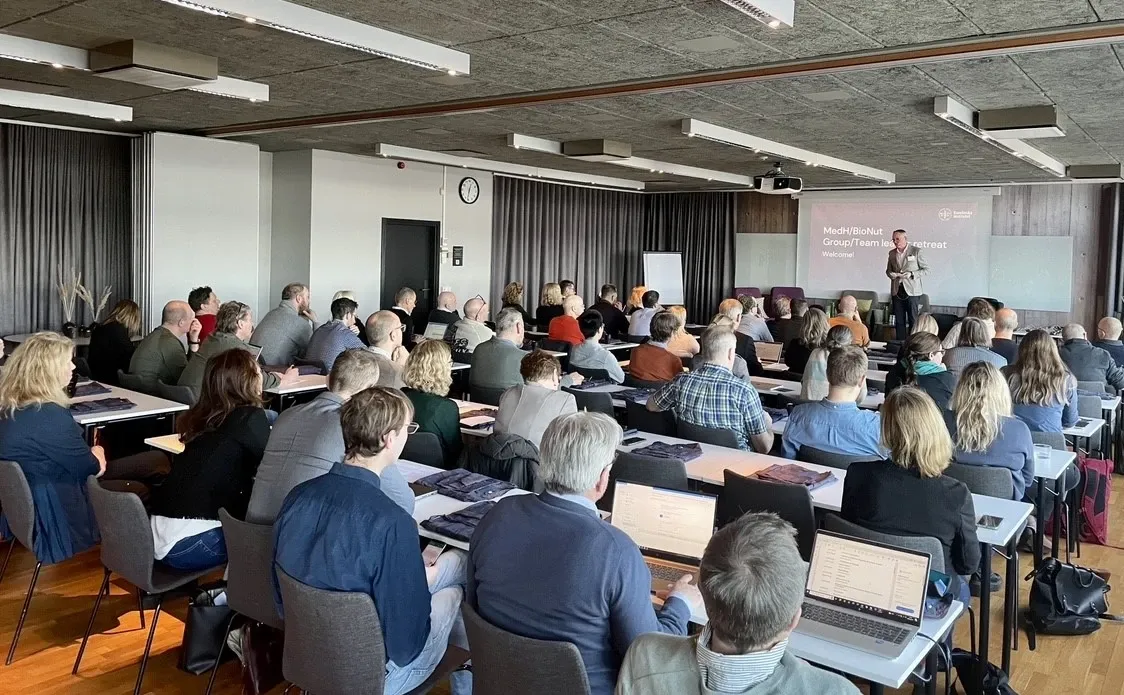 A room of seated people listening to a speaker on stage.