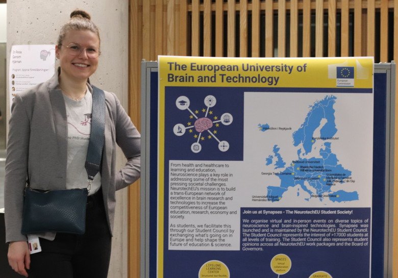 Julia Spielbauer is standing by a poster describing NeurotechEU.