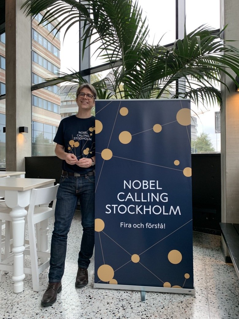 Tobias Alfvén next to roll up with the text Nobel Calling Stockholm