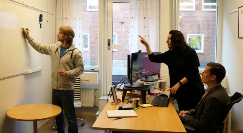 Three people are working on a problem at a whiteboard.