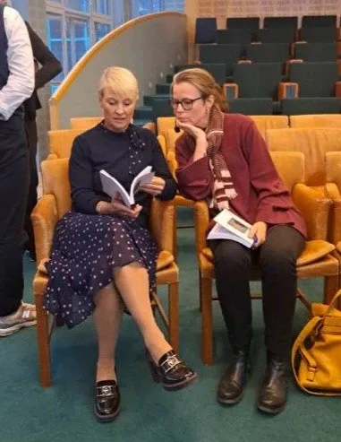 Isabelle von Saenger hands her doctoral thesis to Anna Tenje. They both sit down and Anna Tenje leafs through the book.