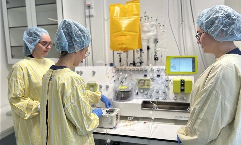 Image depicting a teacher and PhD students in a laboratory, wearing protective clothing.