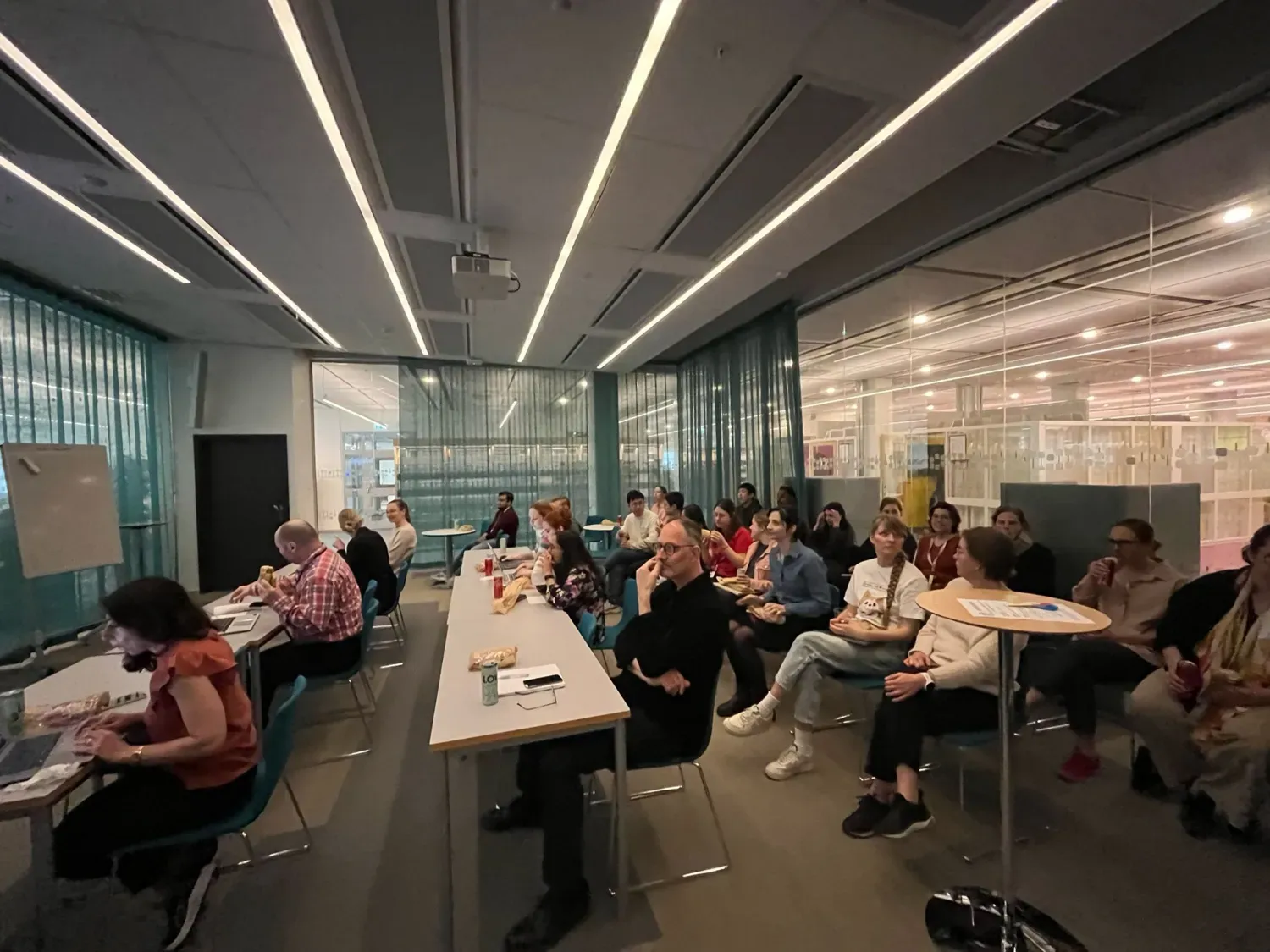 Group photo of people sitting in different rows in a large conference room with glass walls.