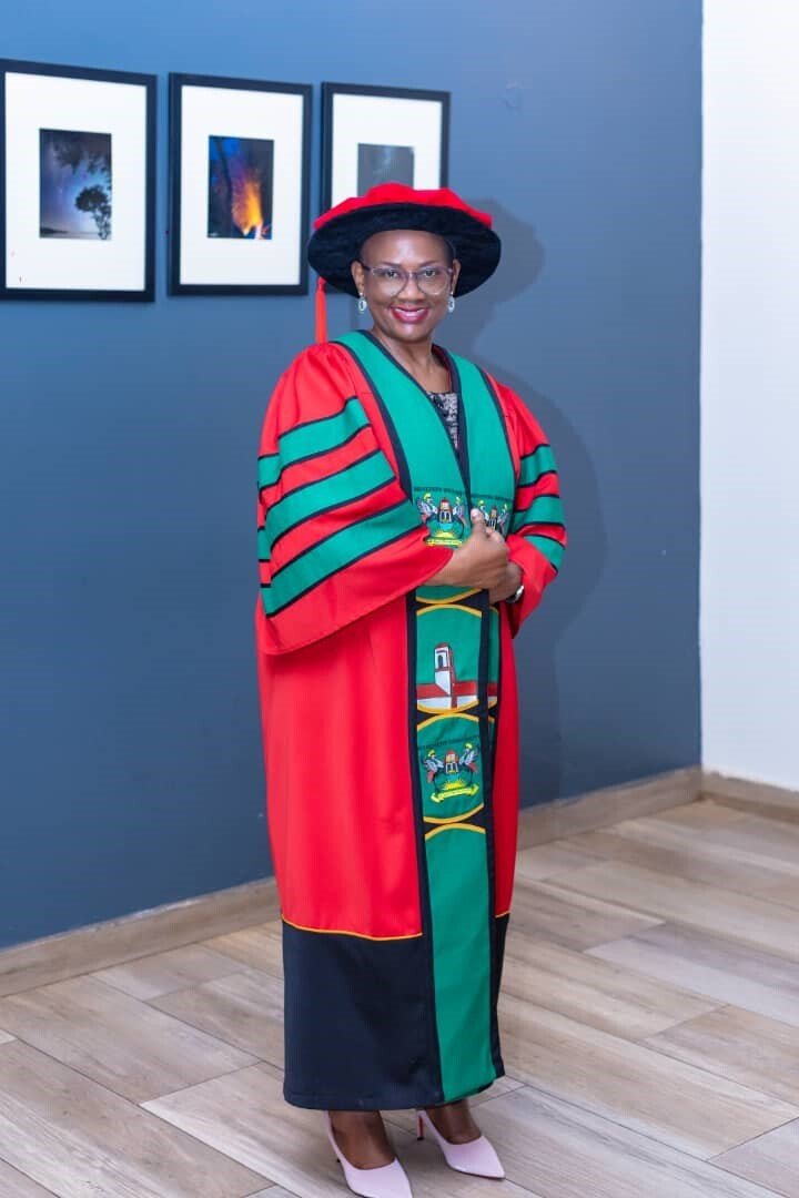 Juliet Mwanga-Amumpaire in a green, red and black colored gown and a red-black hat.