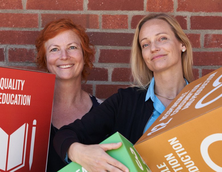 Sara Widén and Hanna Karlsson stand with cubes representing three of the global sustainability goals in front of a brick wall.