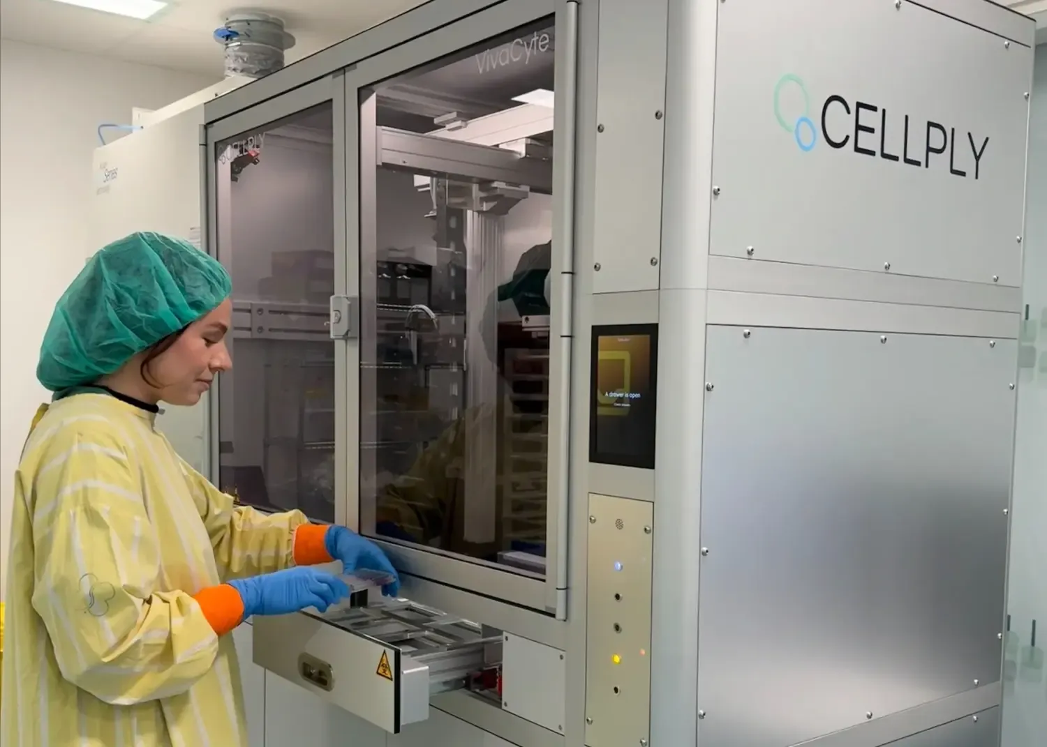 A researcher in a yellow coat stands next to a laboratory machine.