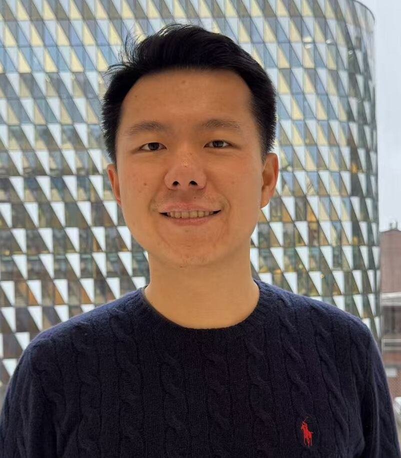 Dark-haired man wearing a blue sweater with Aula Medica in the background.