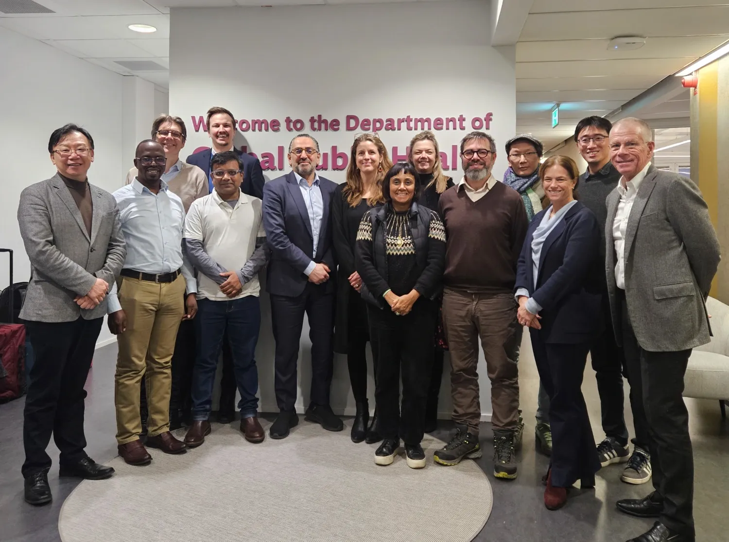 A group of people standing in front of a wall with the text Department of global public health.