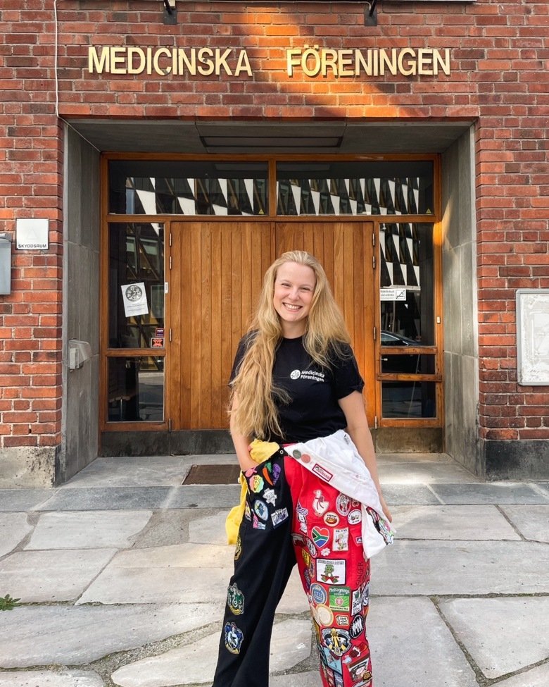 Female student stands smiling in front of the student union building. Medicinska Föreningen is written on the building.