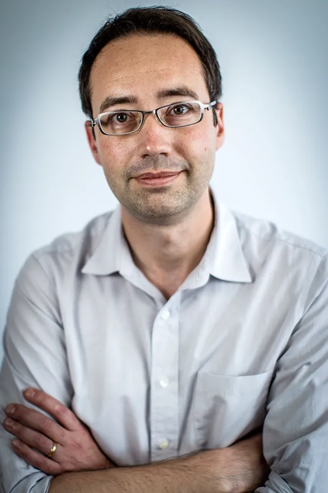 Portrait of a man with dark hair, glasses and arms crossed.