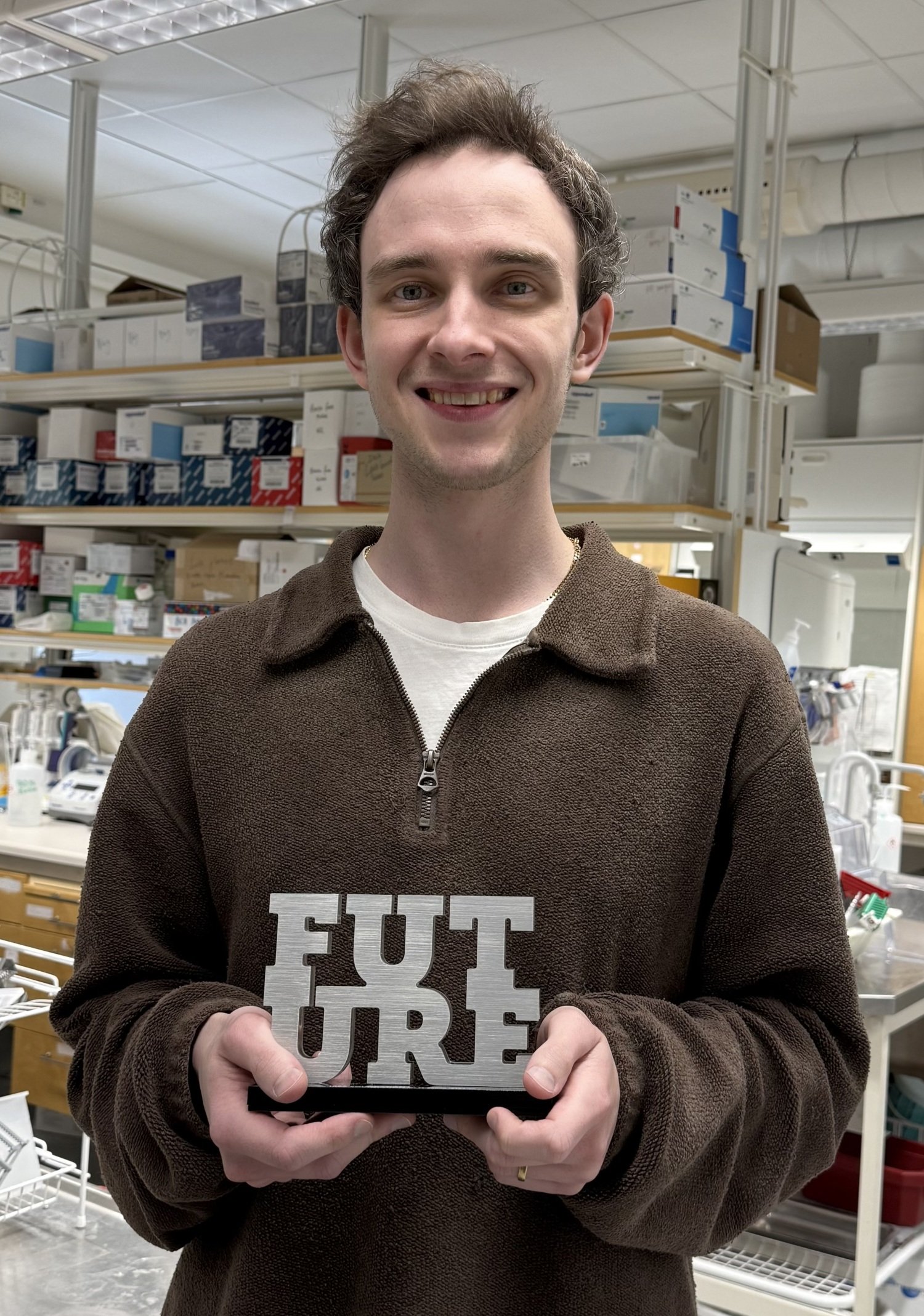Portrait photo of Matthew Hunt, standing in the lab holding his trofe.