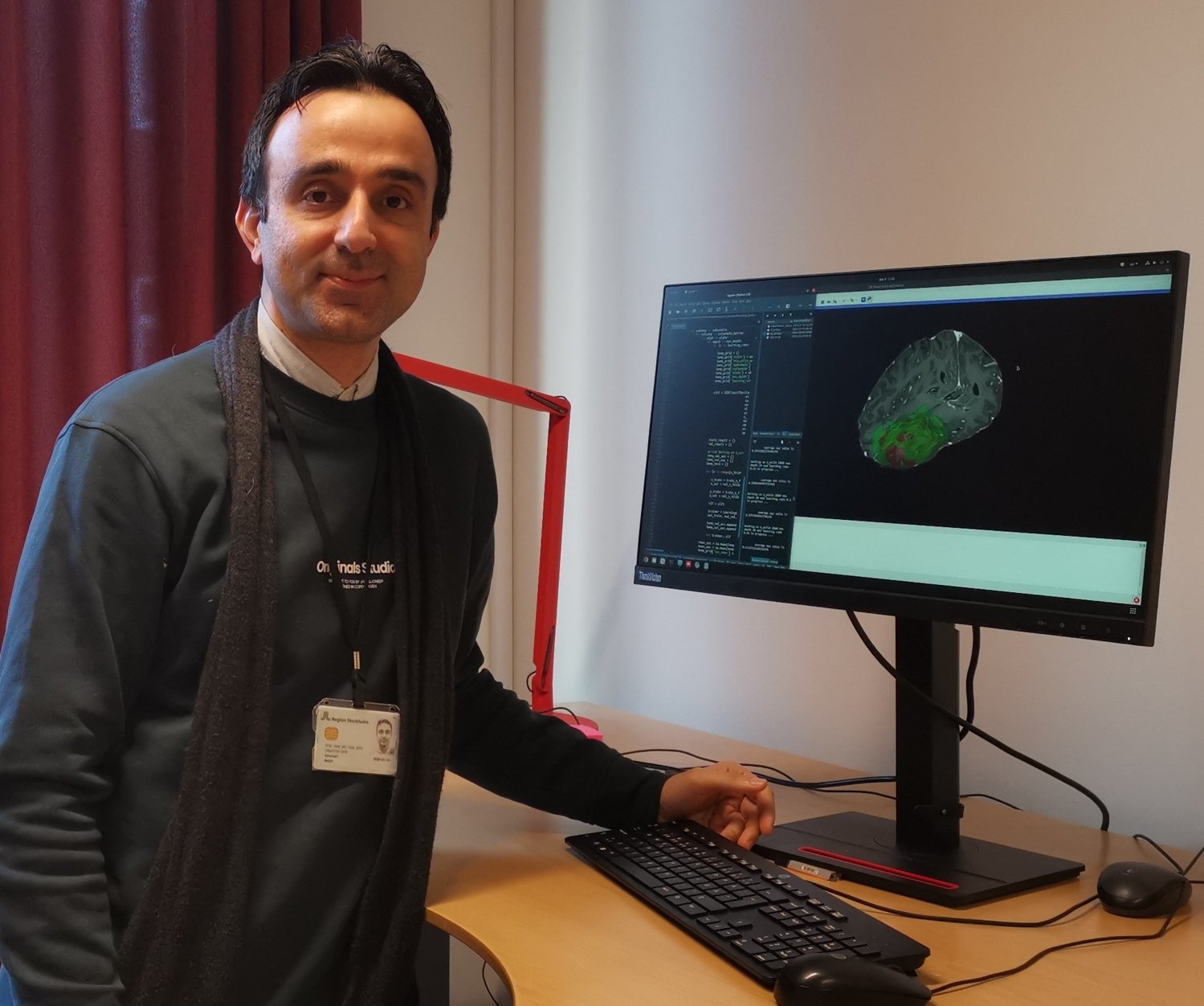 Mehdi Astaraki is standing by a desk with a computer screen showing a 3D image of a brain.