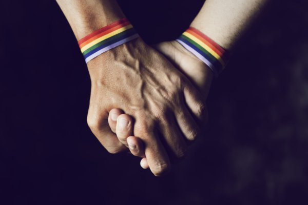 Men holding hands with pride bracelets