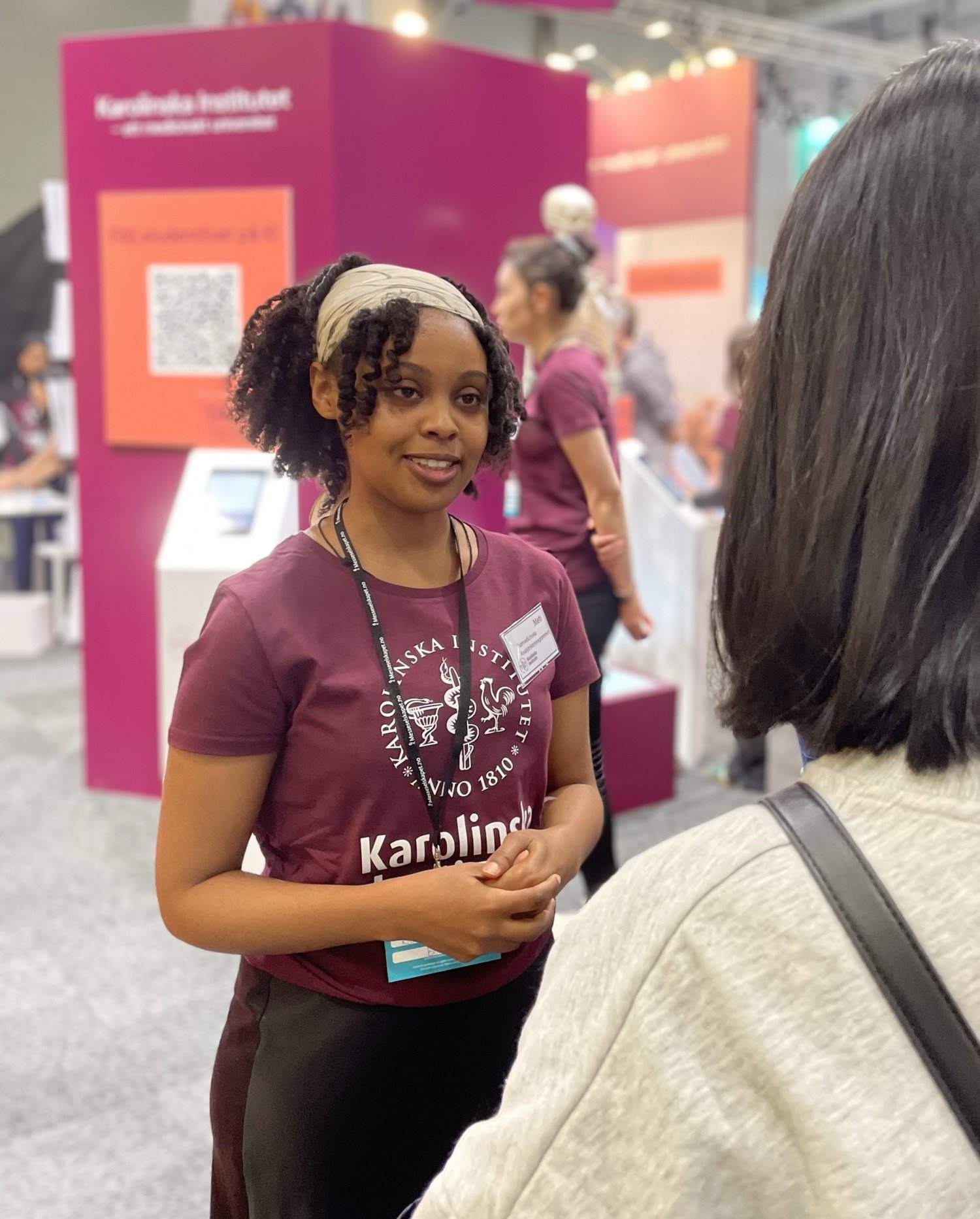 A KI student in a plum red KI t-shirt is talking to a visitor of one of the fairs.