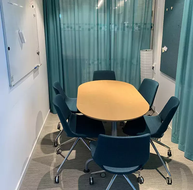 Image of a table and six chairs in a meeting room in ANA Futura. Green curtains surrounds the walls.