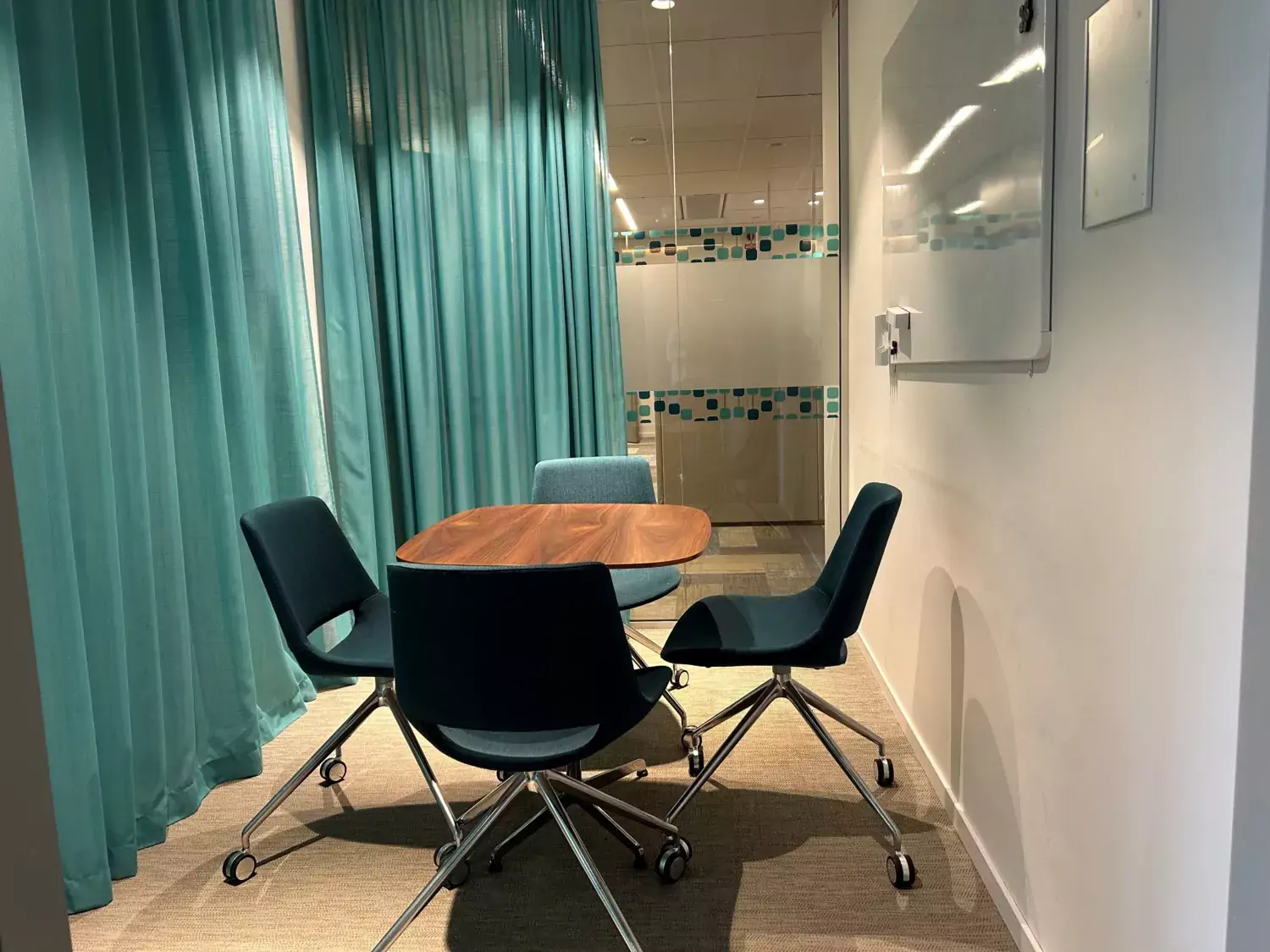 Picture of a meeting room with four blue chairs and a small wooden table. Green thin curtains surround the walls.