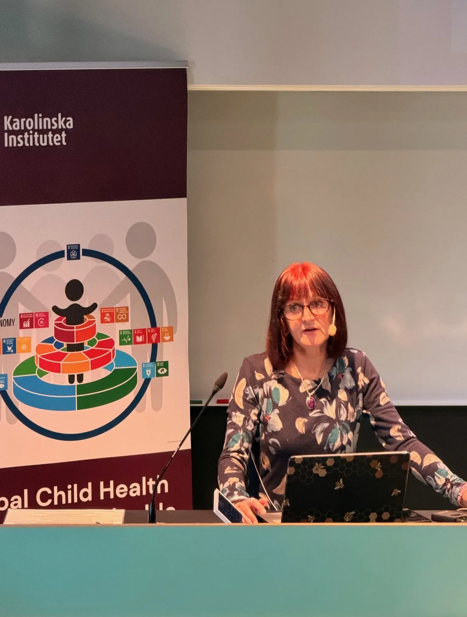 A womanstanding by a podium gving a speach. Beside her is a roll-up with a picture representing the research group Global Child Health.